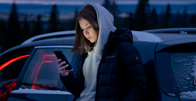 En ung tjej står vi en epa och tittar på sin mobil.