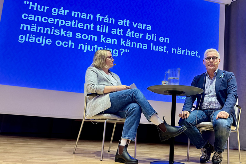 Två personer sitter på en scen vid ett bord och samtalar