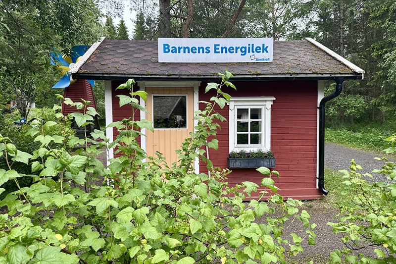 Rödmålad lekstuga med bärbuskar i framkant