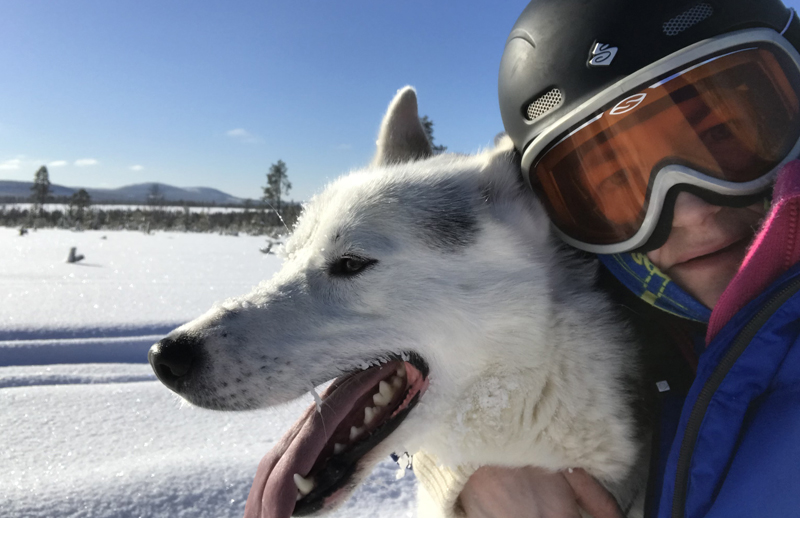 en kvinna med hjälm och skidglasögon kramar om en hund