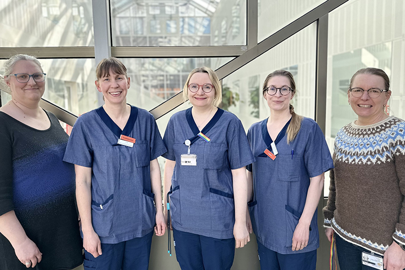 Gruppbild på fem personer som står tätt ihop och ler mot kameran