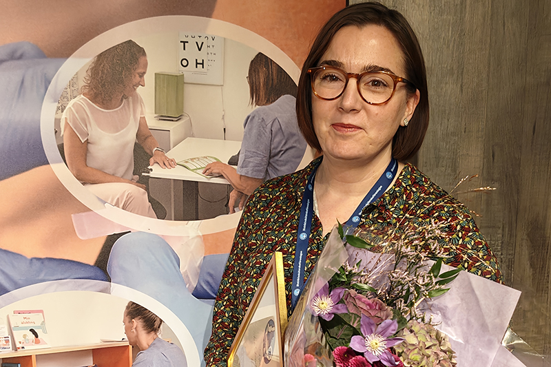 Person i glasögon och med mörkt hår i pagefrisyr. I famnen har personen en blombukett och ett diplom.