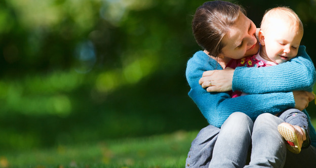 En vuxen person som håller om ett litet barn i en park en solig höstdag.