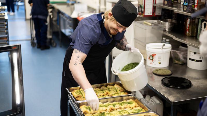 En man sprinklar koriander över enchiladas.