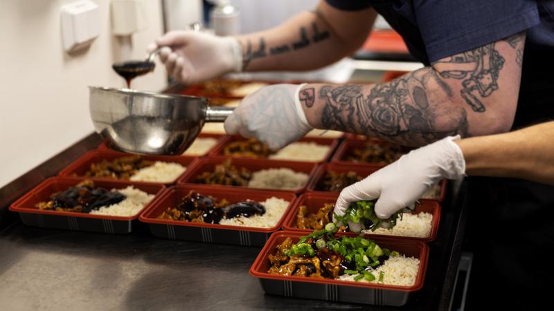Händer lägger på sås och salladslök på mat i matlådor.