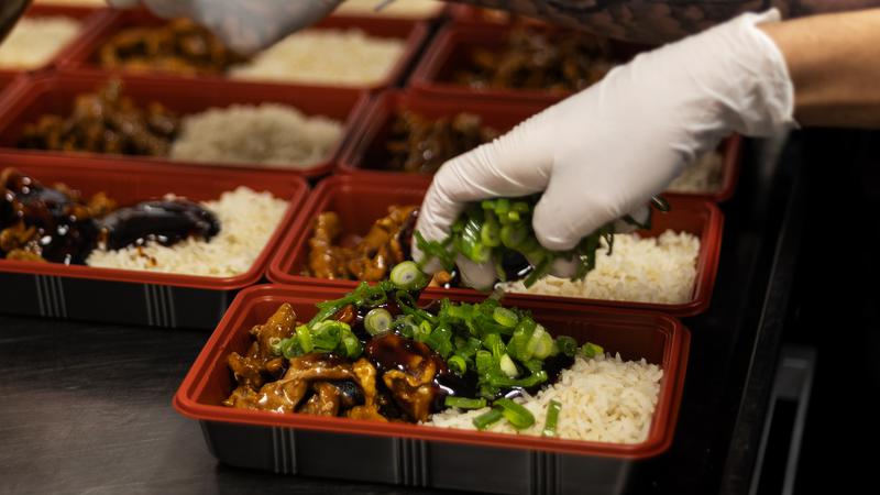 Händer lägger på sås och salladslök på mat i matlådor.