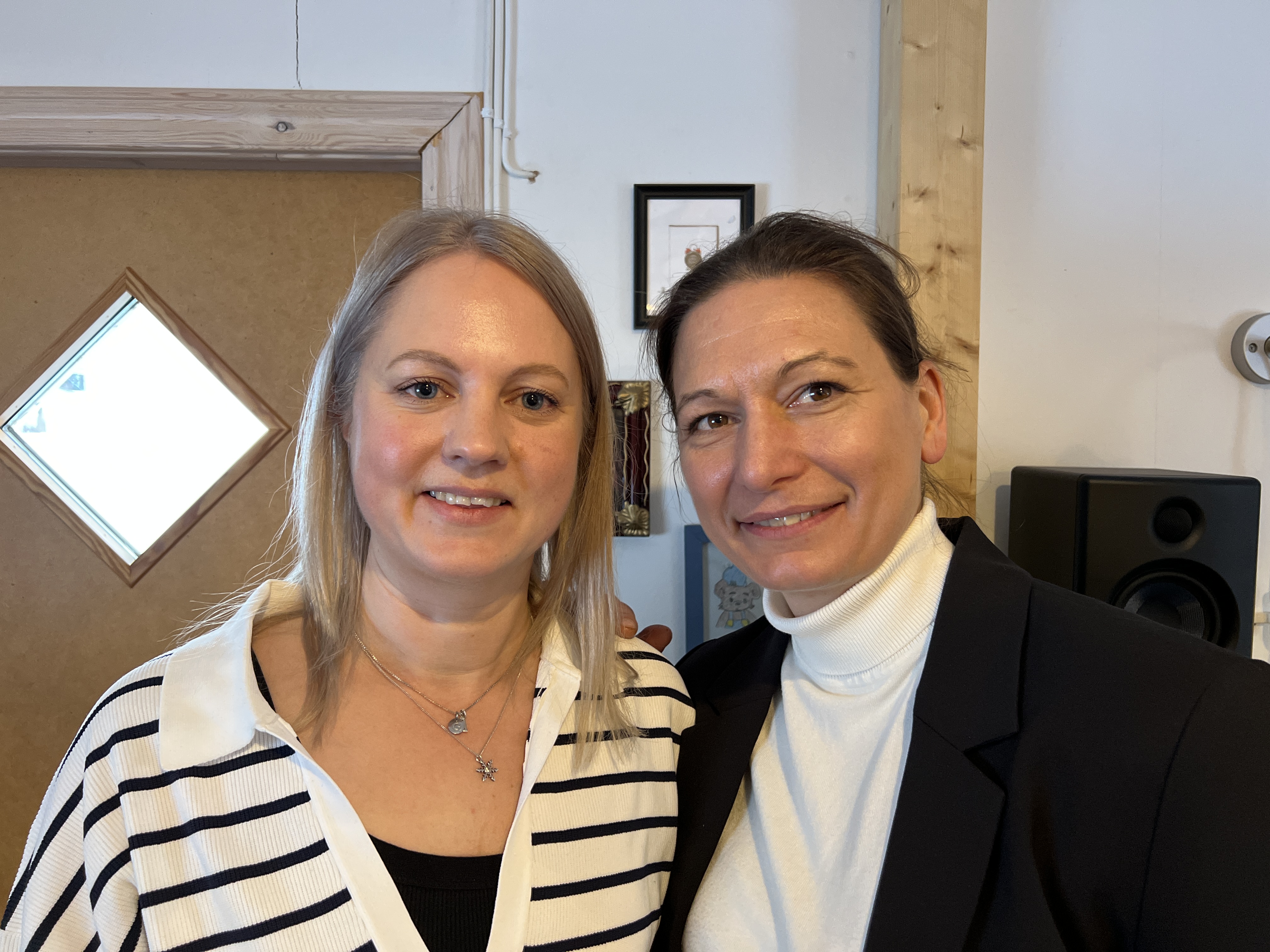 Två leende personer, en blond med stickad kofta och en brunhårig med kavaj och vit tröja.