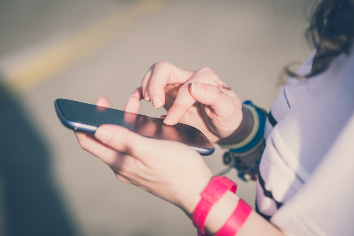 Närbild på ung persons händer som skriver på en mobiltelefon.