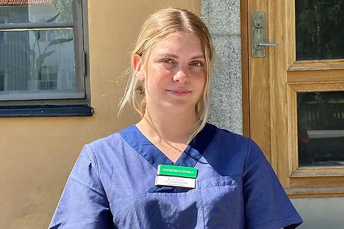 En person i blåa vårdkläder tittar in i kameran.