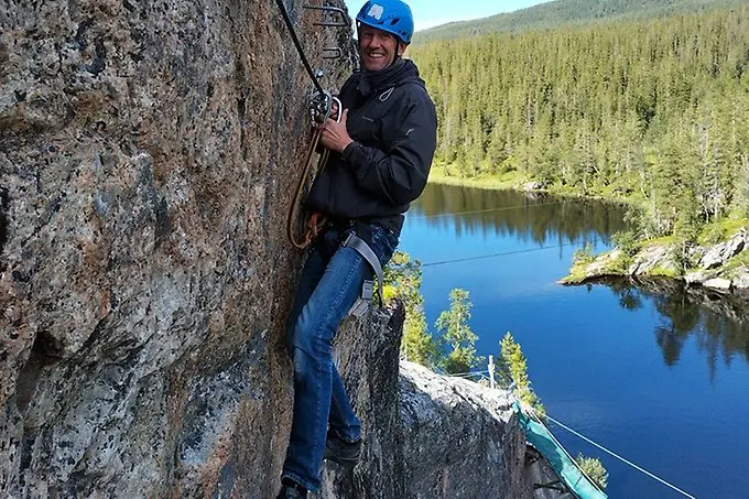 En leende person, klättrandes på en bergvägg, tittar in i kameran.