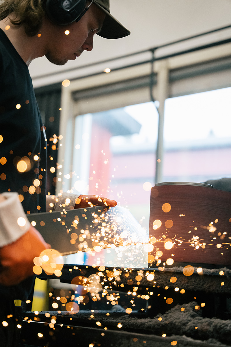 Närbild på ett par skidor vars stålkanter dras mot en slipmaskin, med glöd som sprutar runt den.