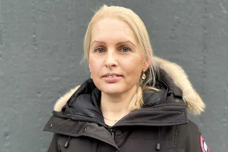 En person i vinterjacka med blont hår uppsatt i en hästsvans tittar in i kameran