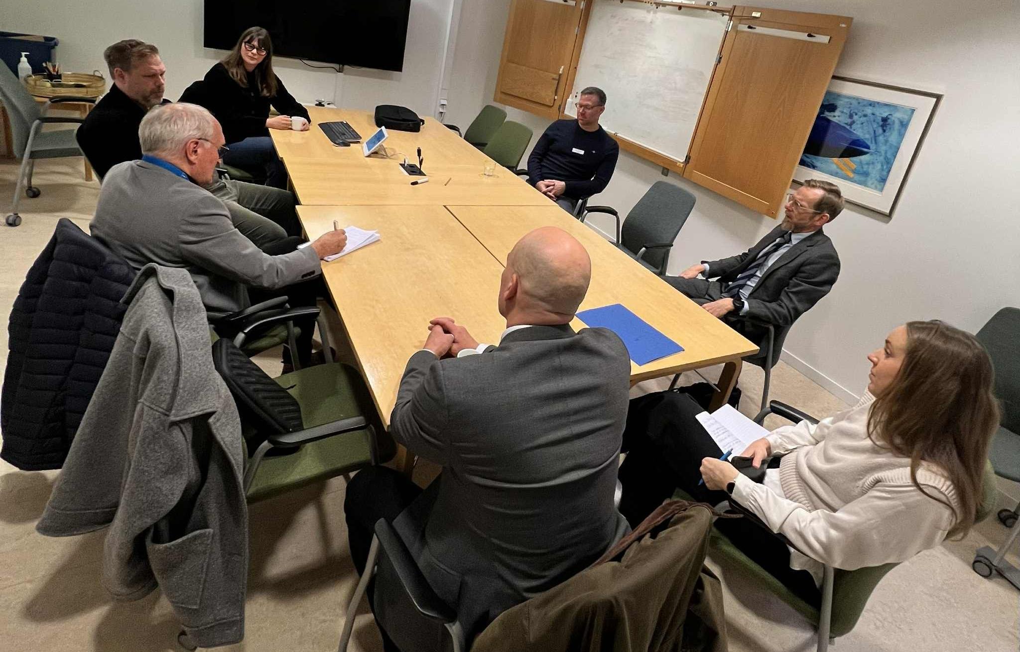 Sju personer sitter runt ett bord och pratar. 