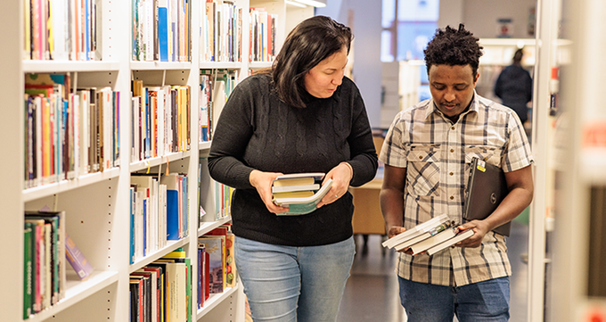 Två personer med böcker i ett bibliotek