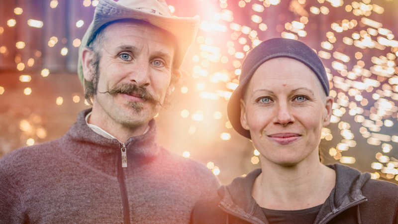 Två personer står framför en mönstrad bakgrund.