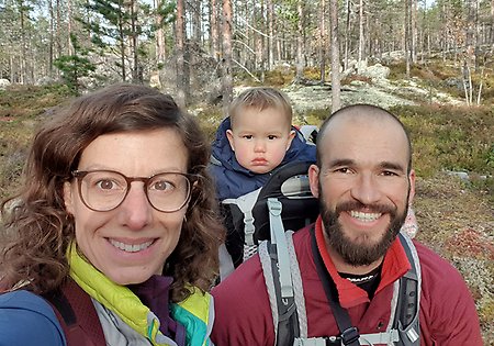 Två personer i skogen En av personerna bär ett barn på ryggen 